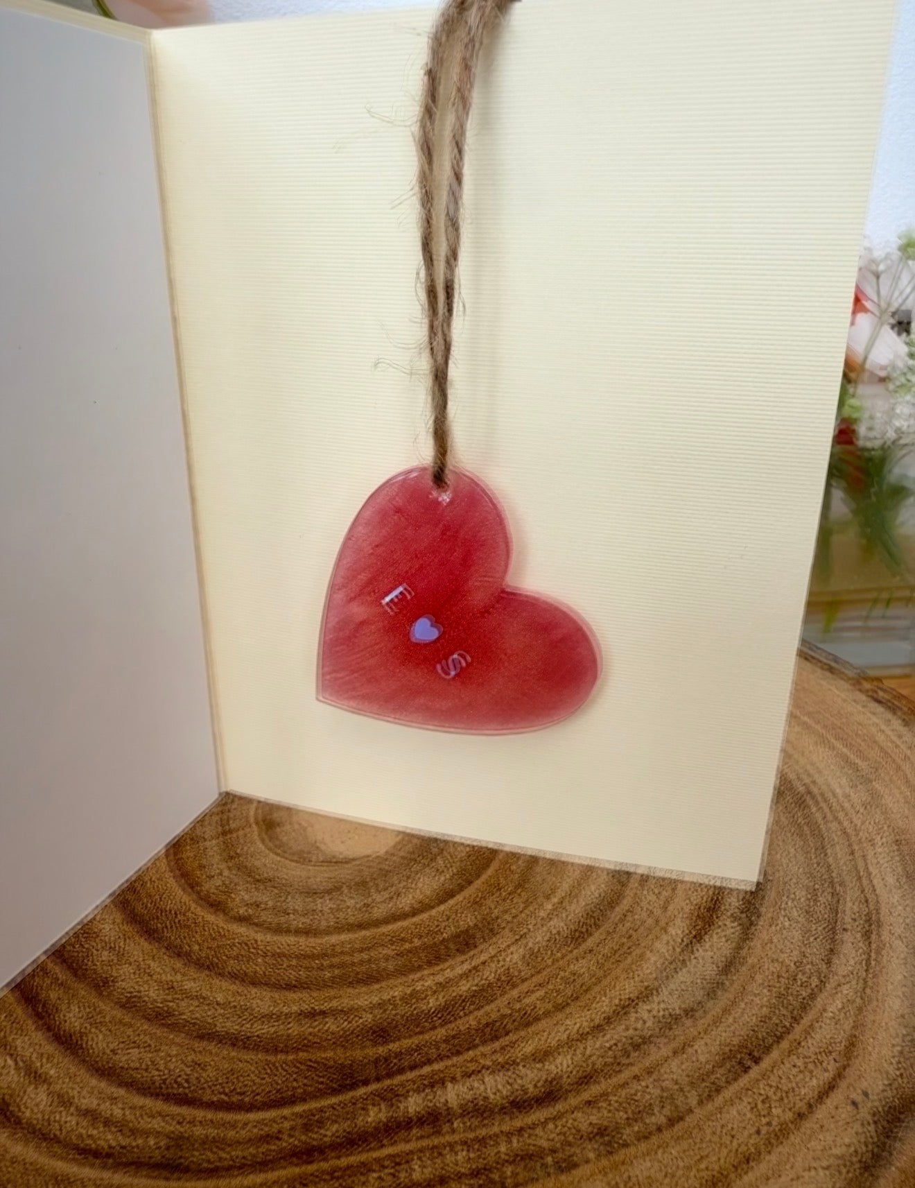 Red heart-shaped tag with a smiley face on a white card with brown string, placed on a wooden surface.