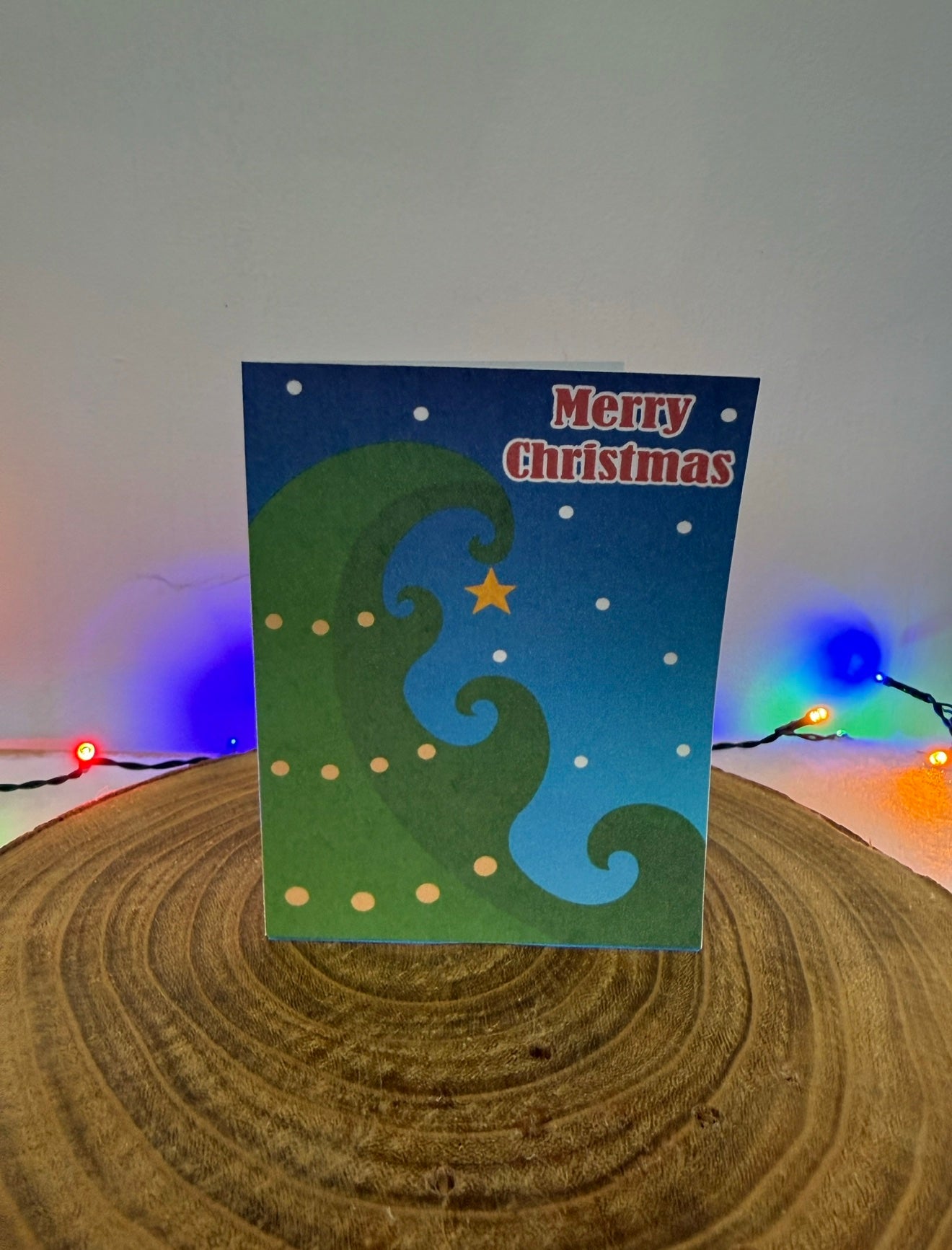 Christmas card with wavy design and star on a wooden surface with colorful lights.
