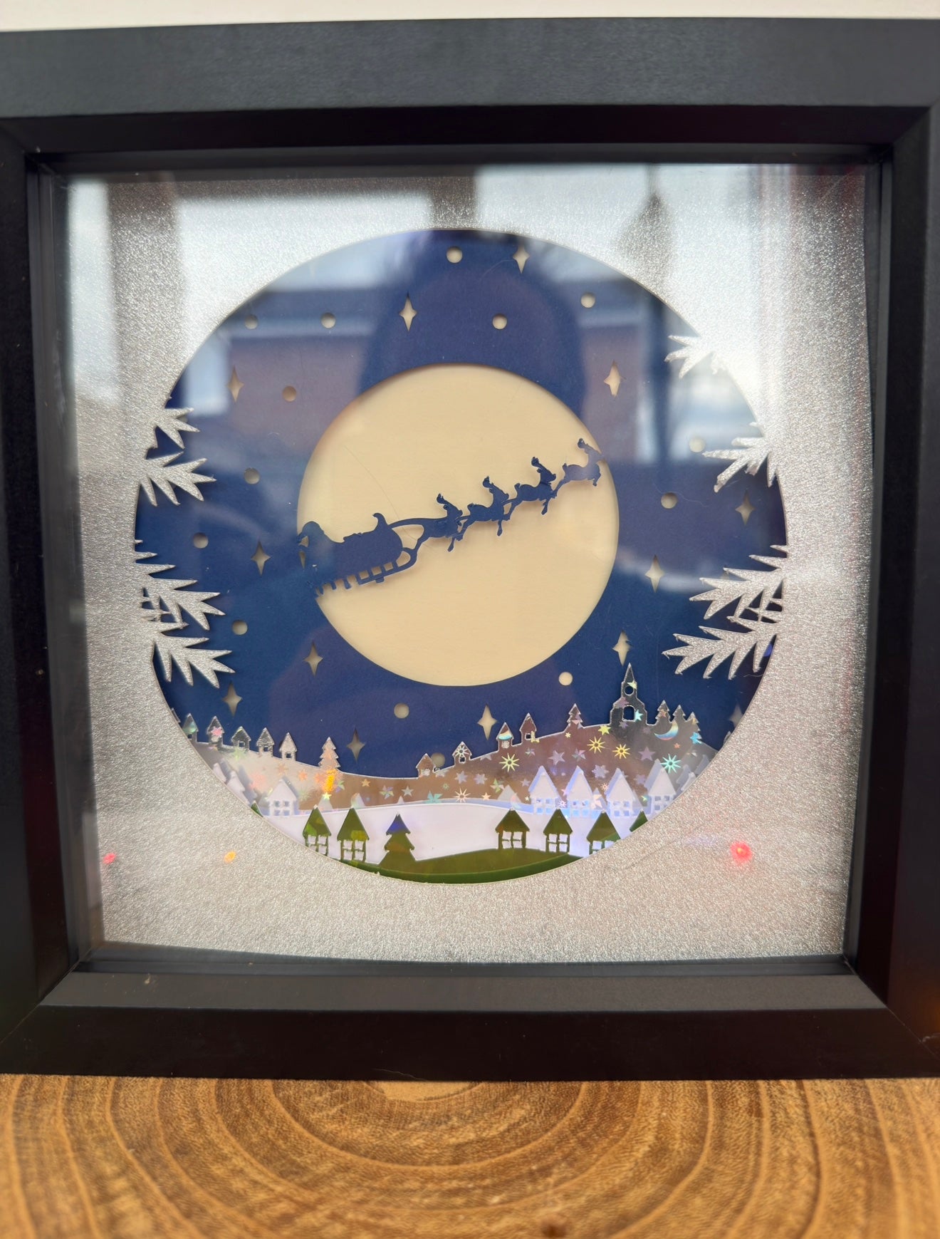Framed artwork of Santa Claus in a sleigh against a moonlit sky with a town below.