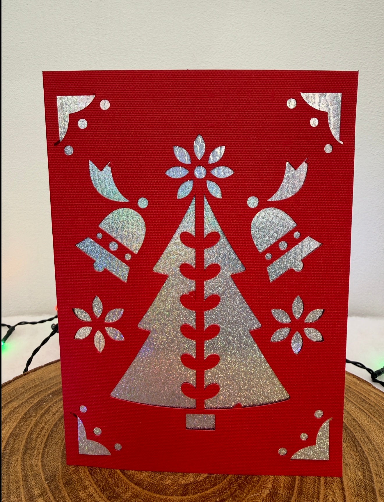 Red card with silver Christmas tree and bell design on a wooden surface.