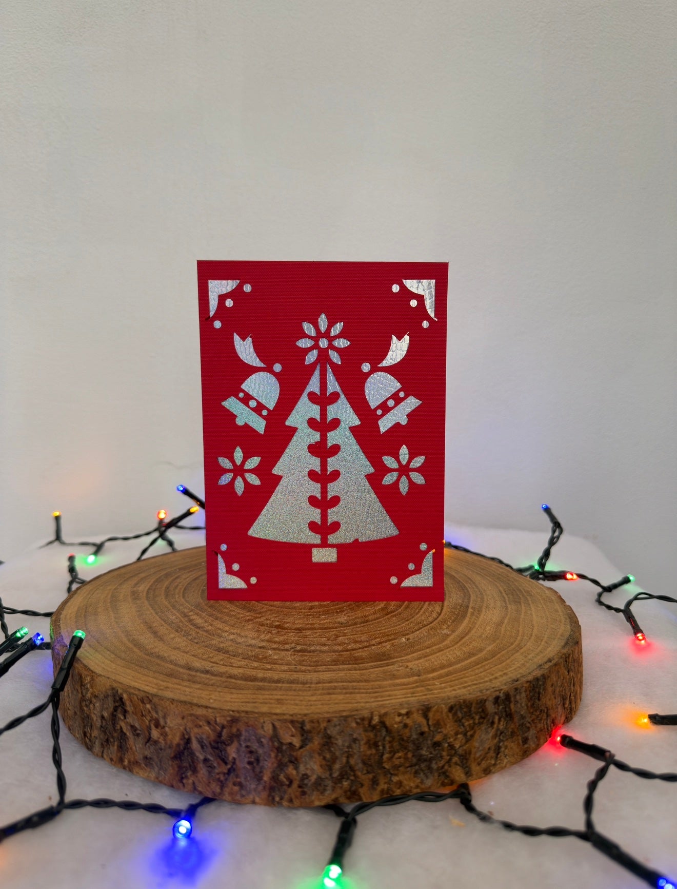 Red card with white tree design on a wooden stand with Christmas lights in the background