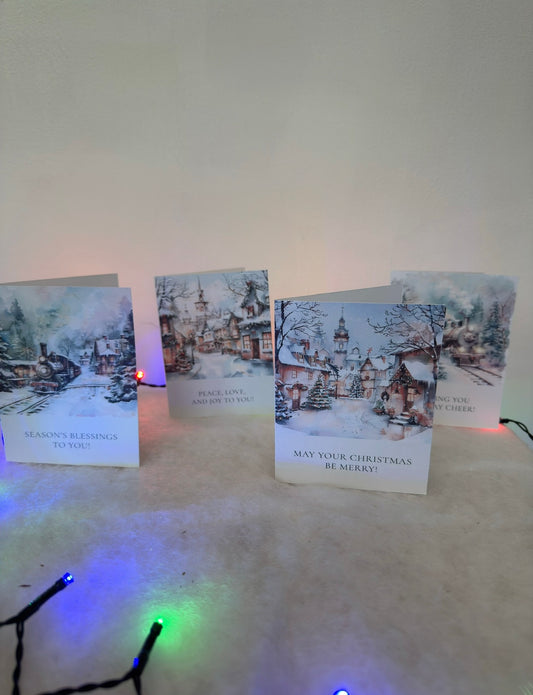 Set of Christmas cards with snowy village scenes on a white surface with colorful lights.