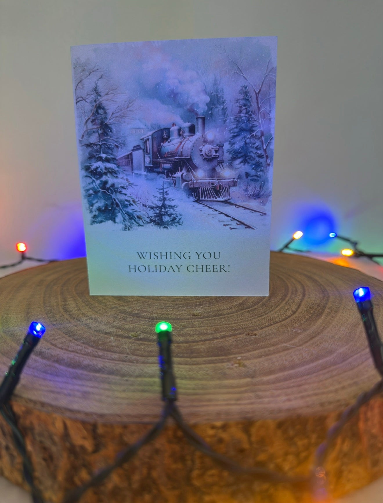 Holiday card with a train scene on a wooden stand with string lights.