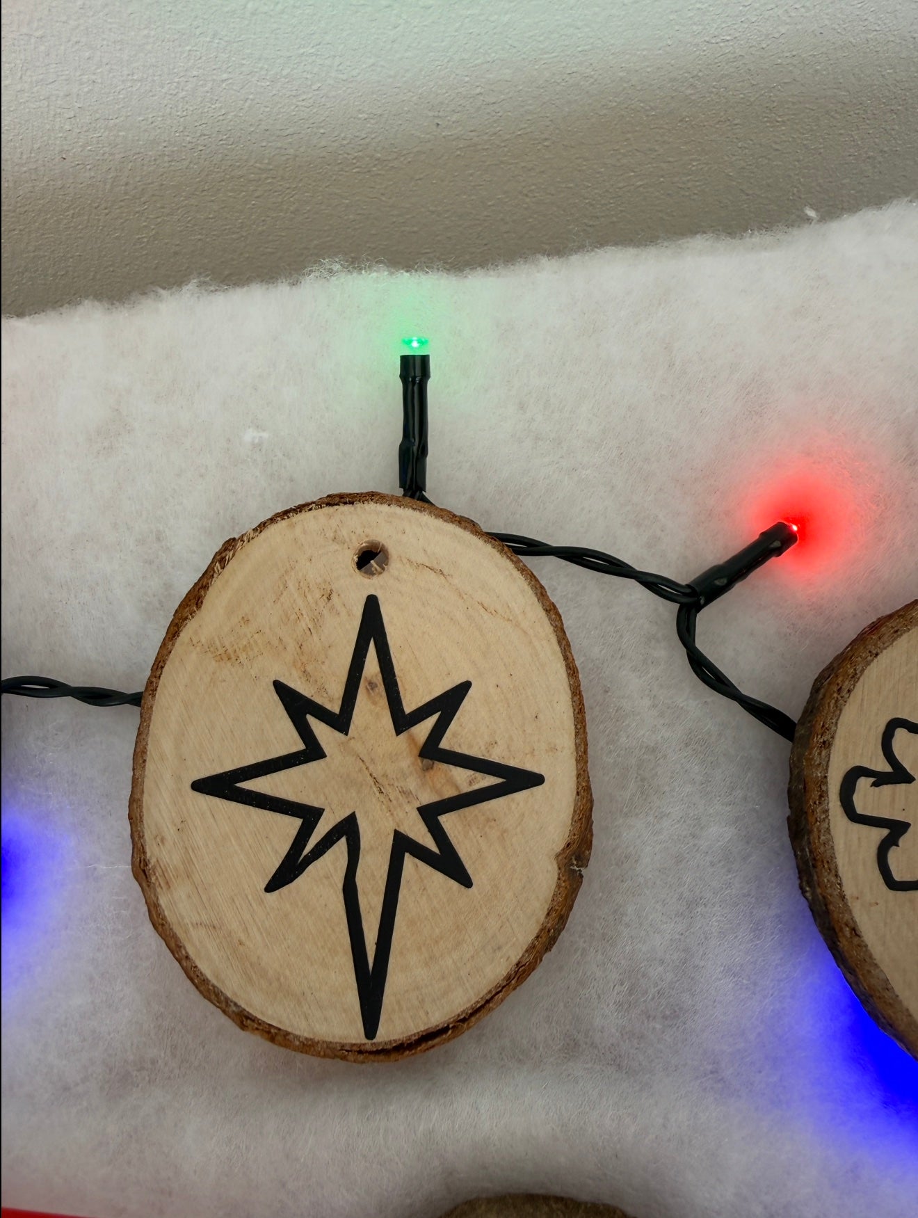 Wooden ornaments with star designs on a snowy background with string lights.