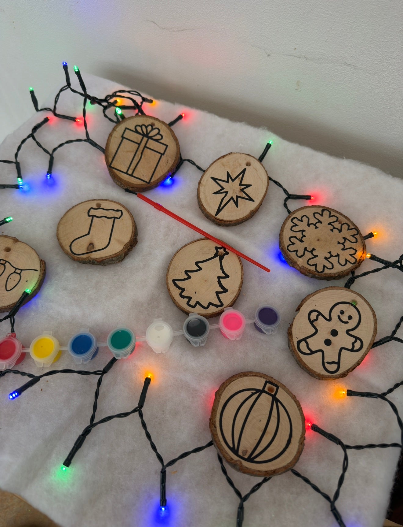 Wooden ornaments with Christmas designs and string lights on a white surface