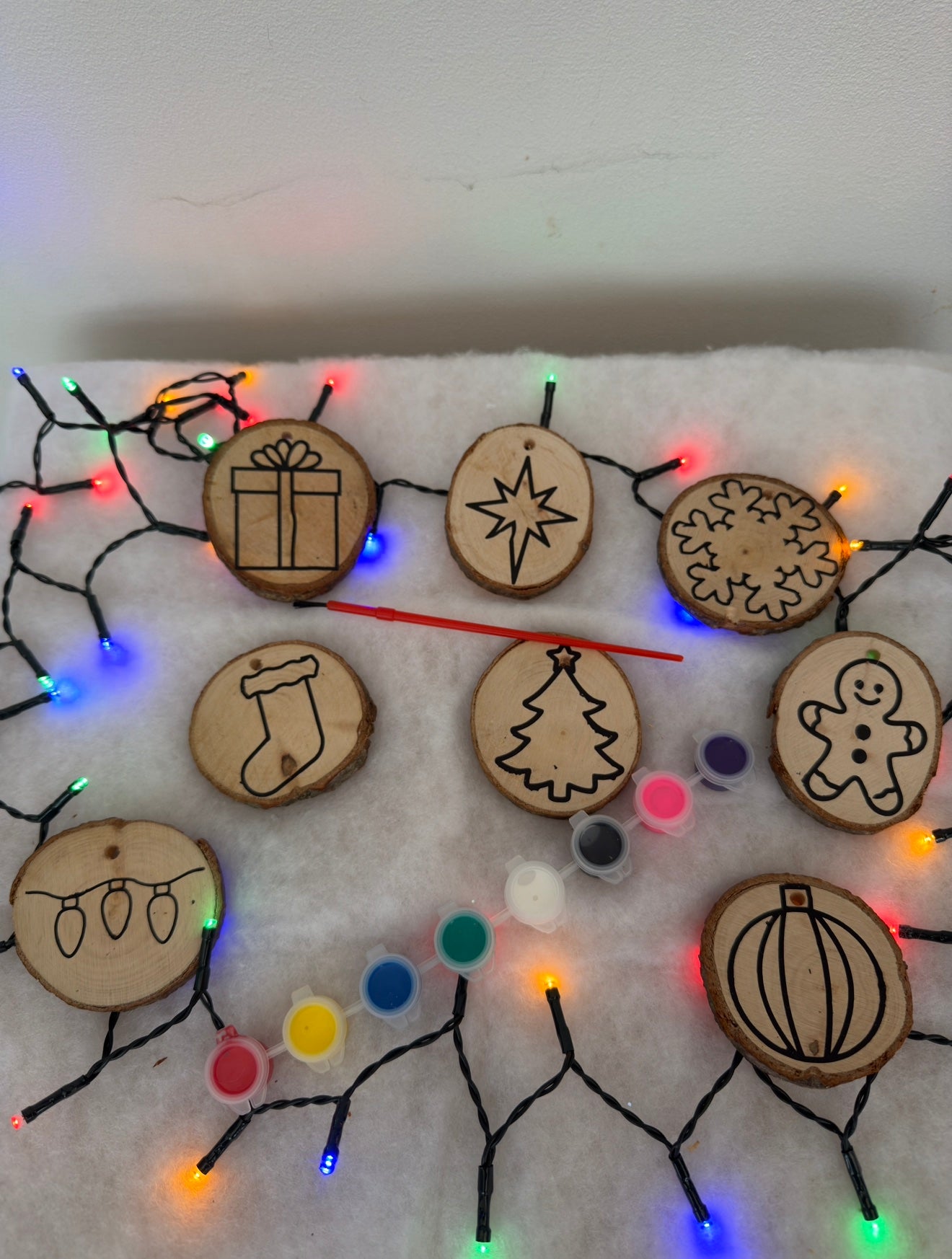 Wooden Christmas ornaments with engraved designs on a white surface with colorful lights.