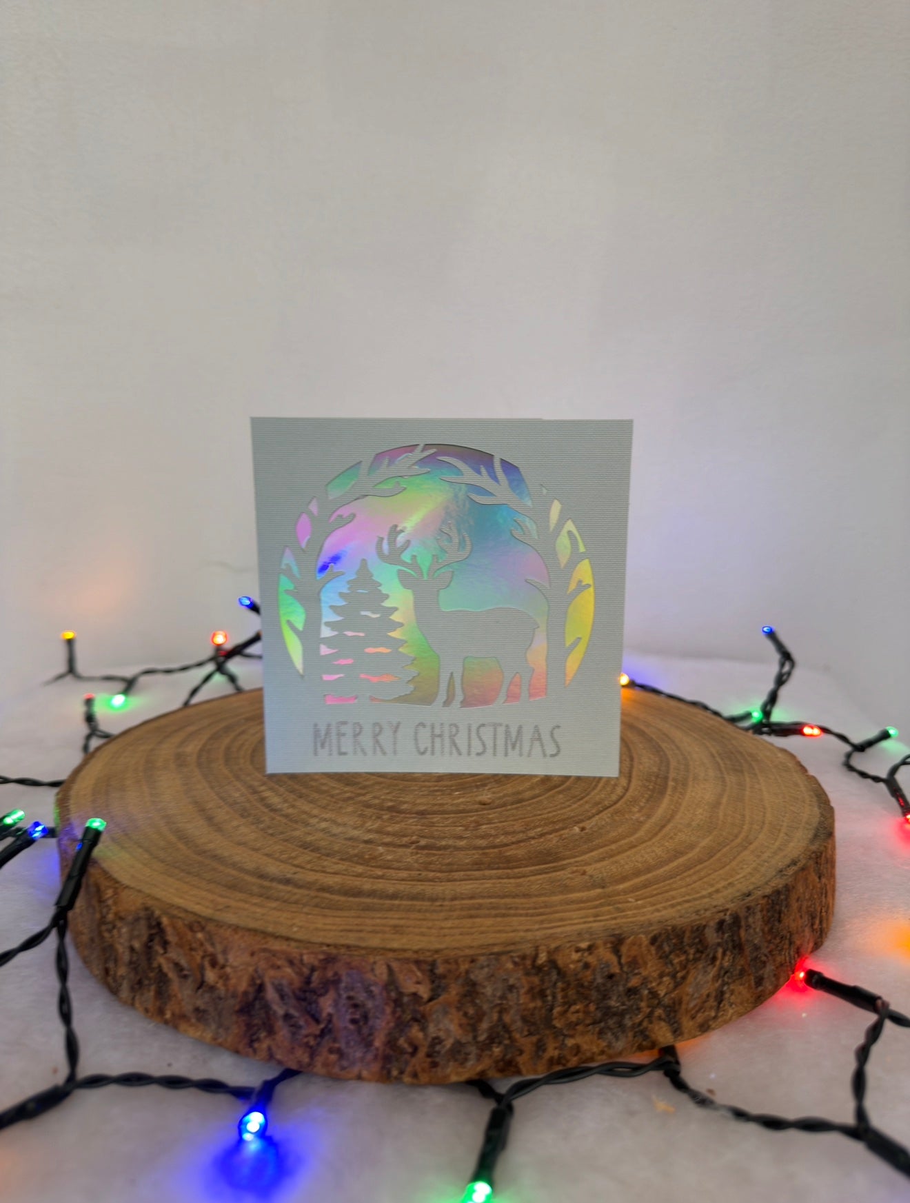 Holographic Christmas card on a wooden stand with string lights in the background