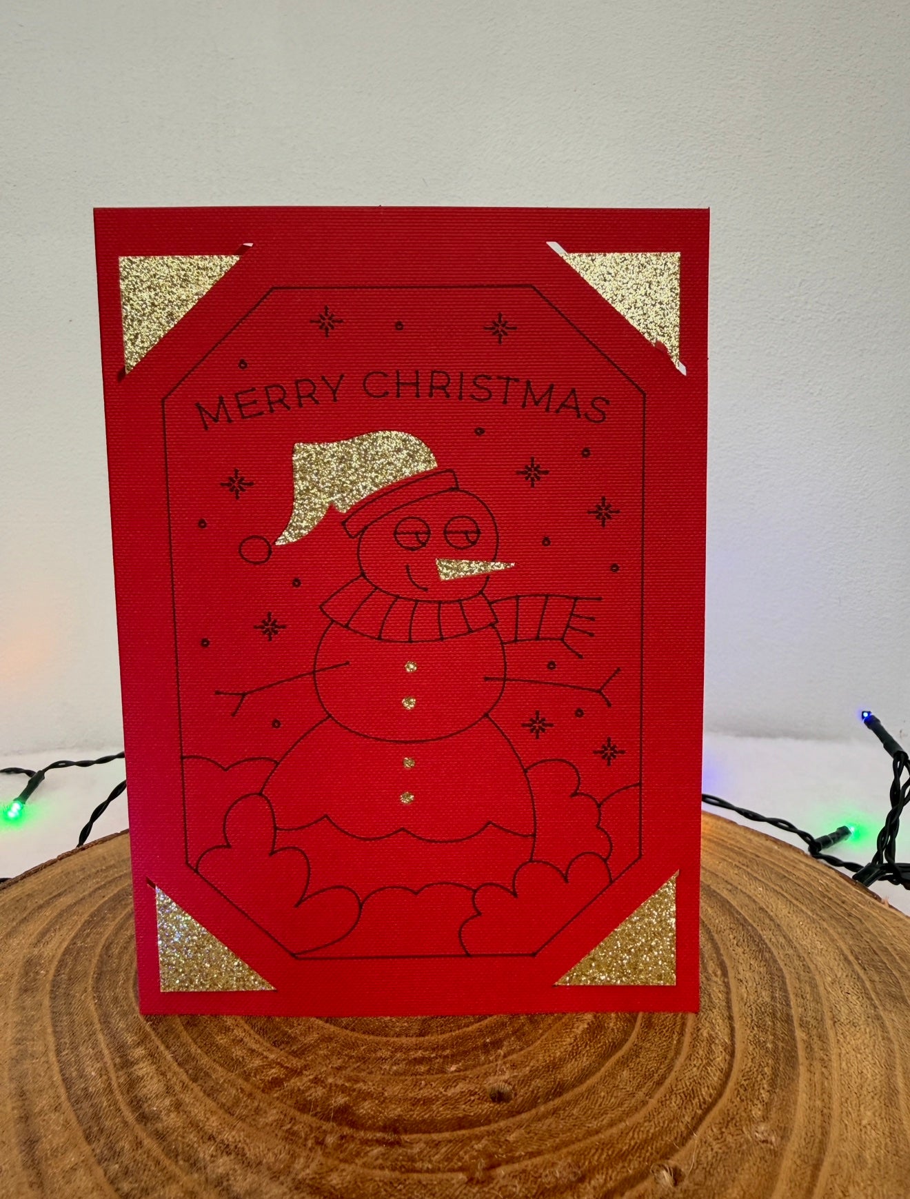 Red Christmas card with a snowman design and 'Merry Christmas' text on a wooden surface.