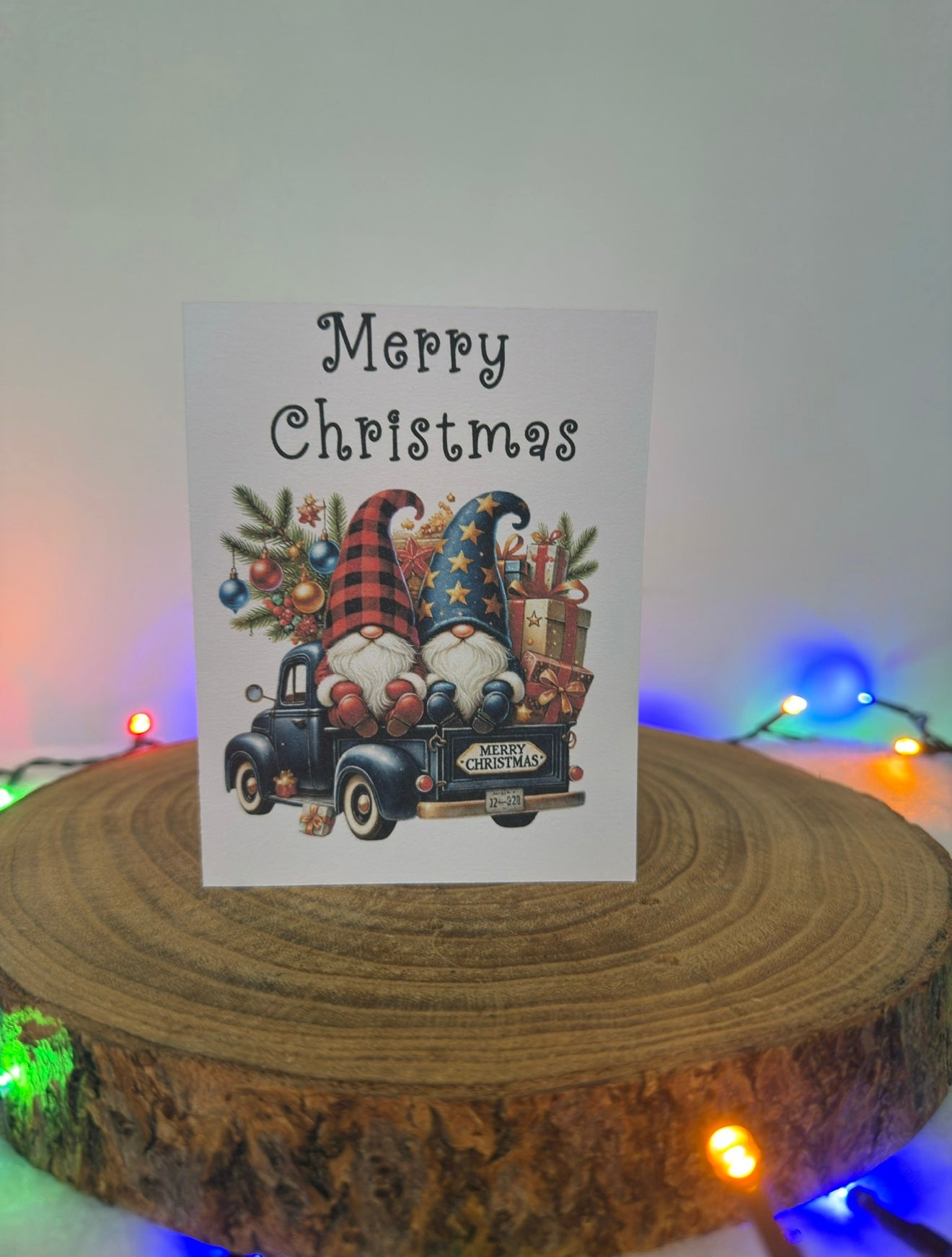 Christmas card with gnomes and truck on a wooden block with festive lights in the background